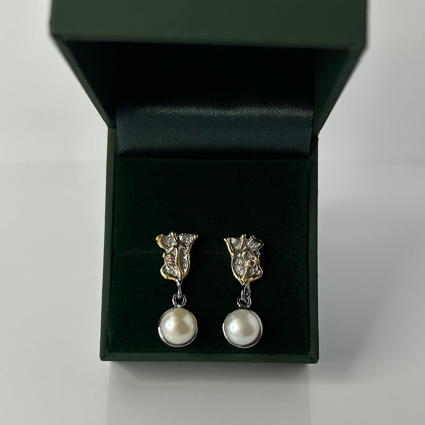 Pair of pearl earrings in a green jewelry box on a light gray background