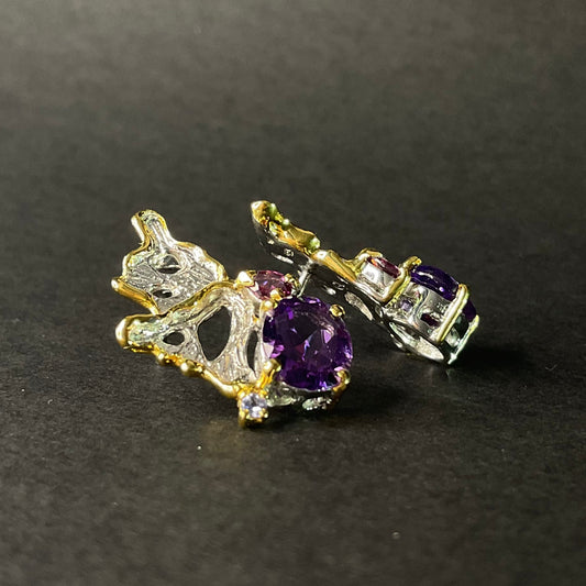 Pair of silver gold earrings with purple amethyst gemstones on a dark background