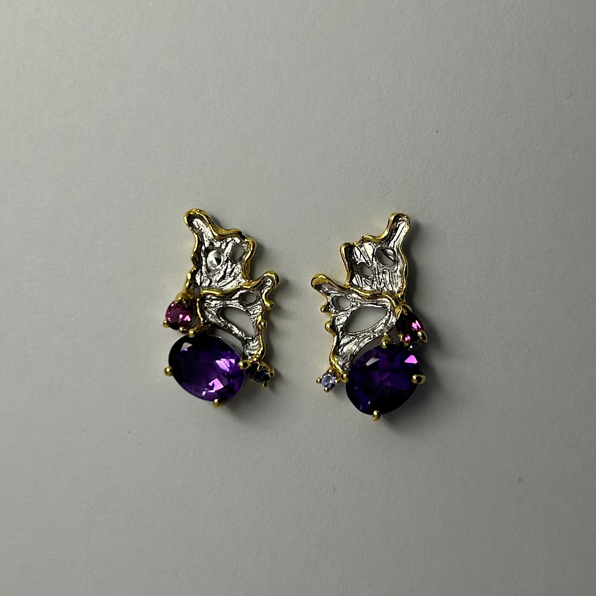 Pair of gold and silver earrings with purple amethyst gemstones on a light gray background