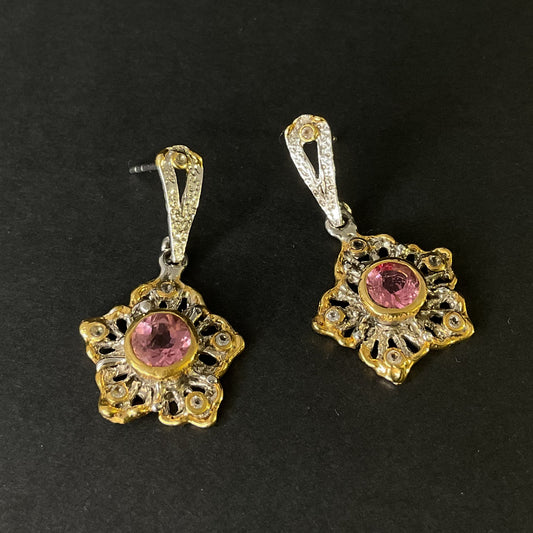 Pair of gold and silver earrings with pink gemstones on a black background