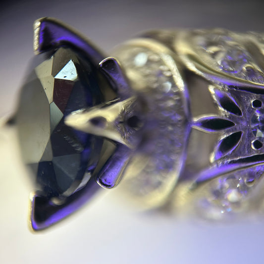 Close-up of a decorative silver ring with intricate designs and a purple sapphire.