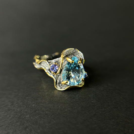 Gold and silver ring with blue topaz gemstone on a black background