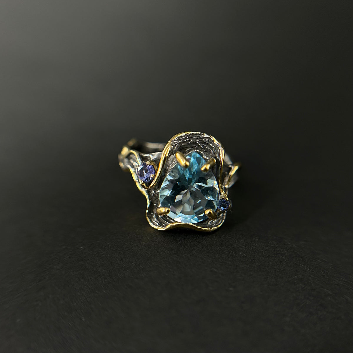 Gold and silver ring with a blue topaz gemstone on a black background