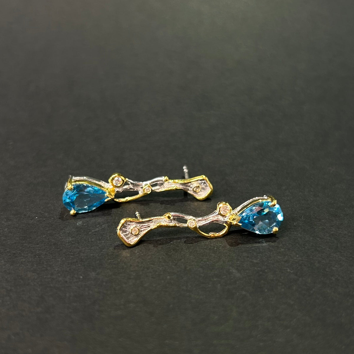 Pair of gold and silver earrings with blue topaz gemstones on a black background