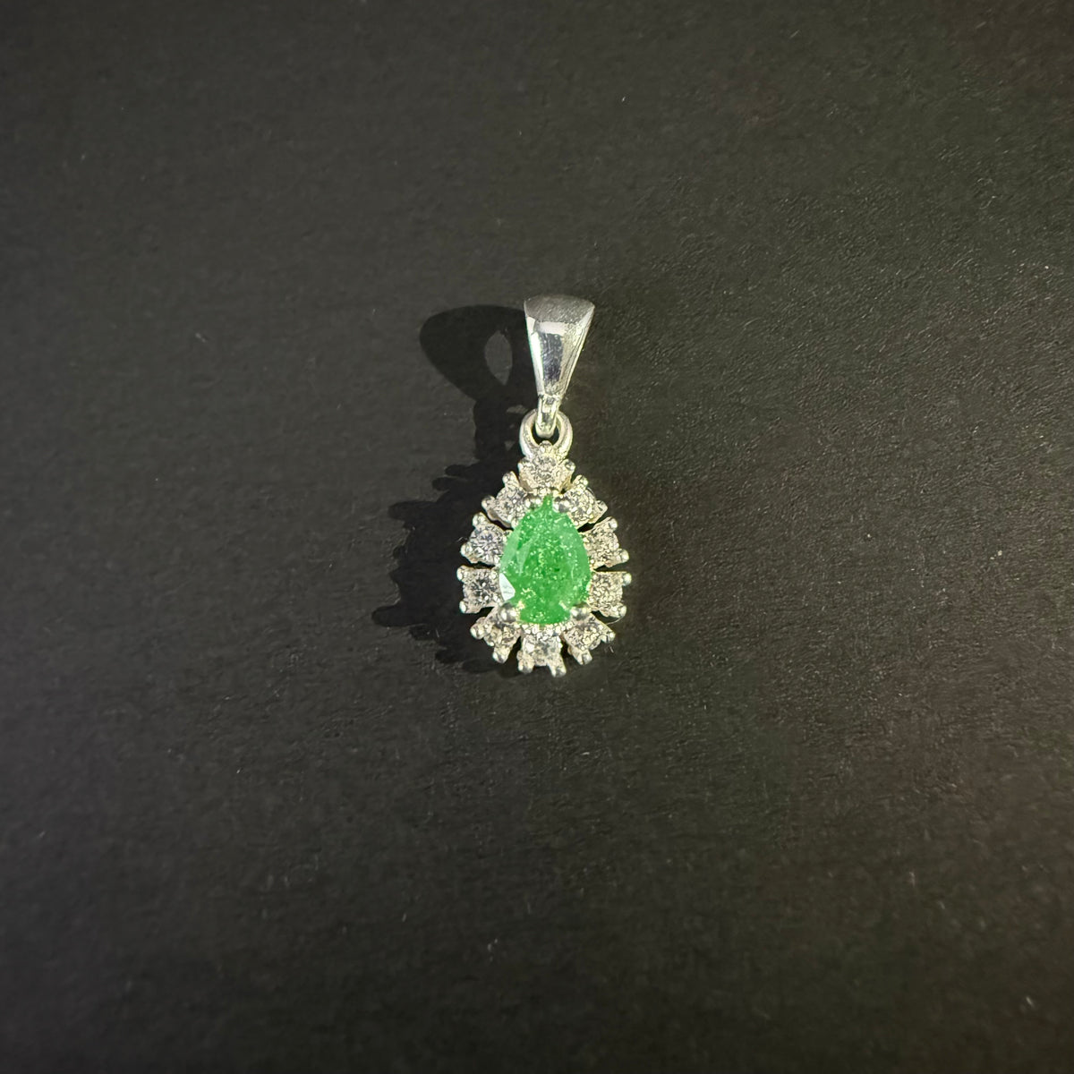 A silver pendant featuring a central green teardrop-shaped gemstone surrounded by a halo of small clear stones