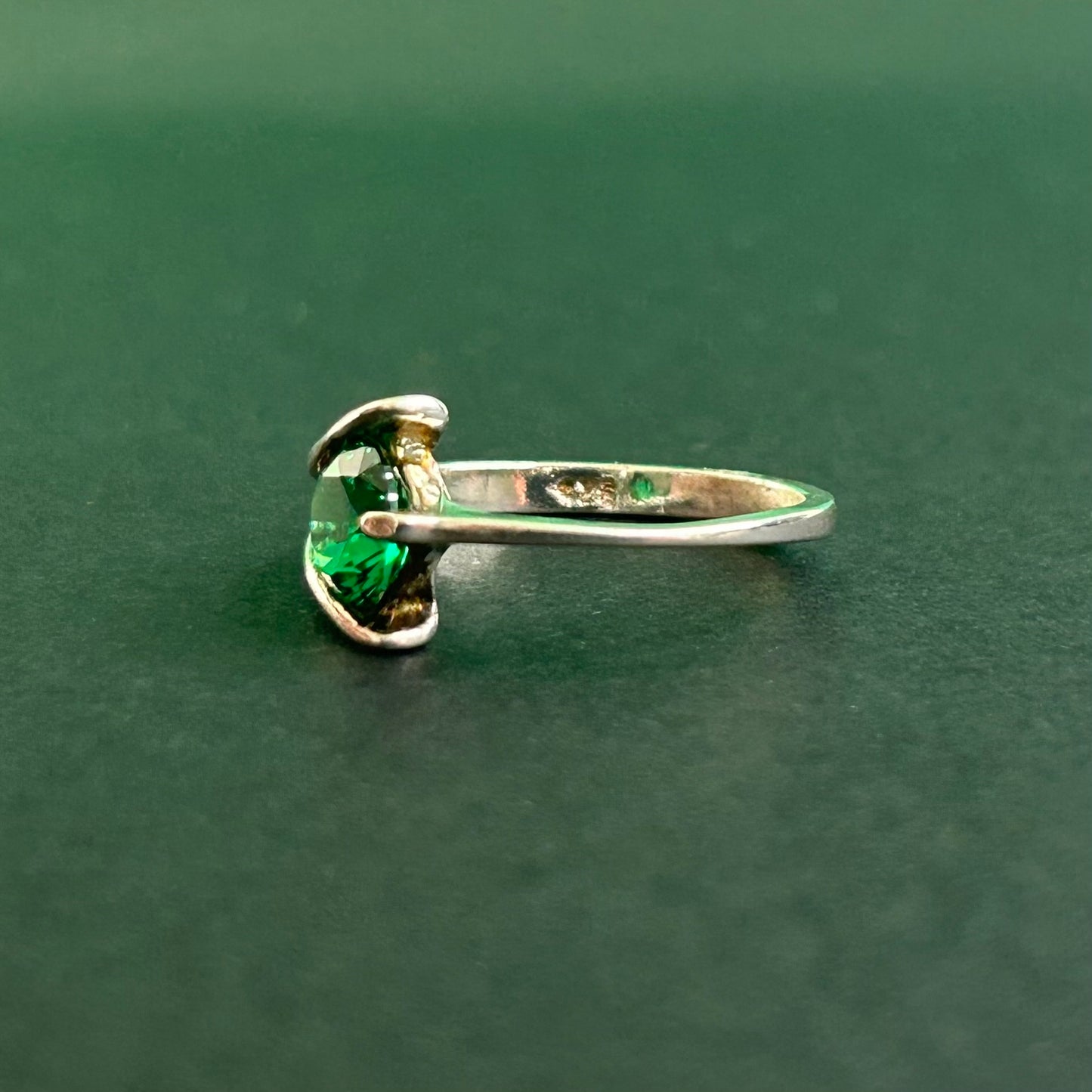 Silver ring with a green gemstone on a dark green background