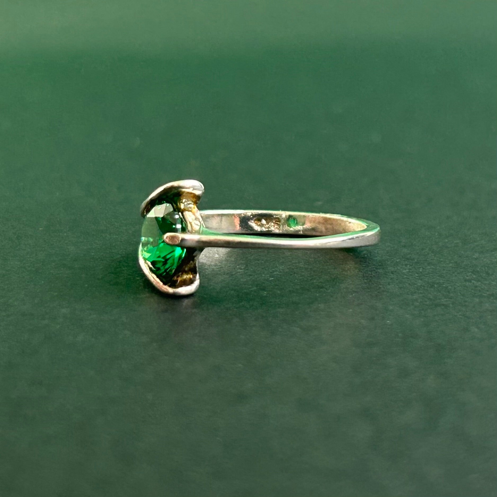Silver ring with a green gemstone on a dark green background