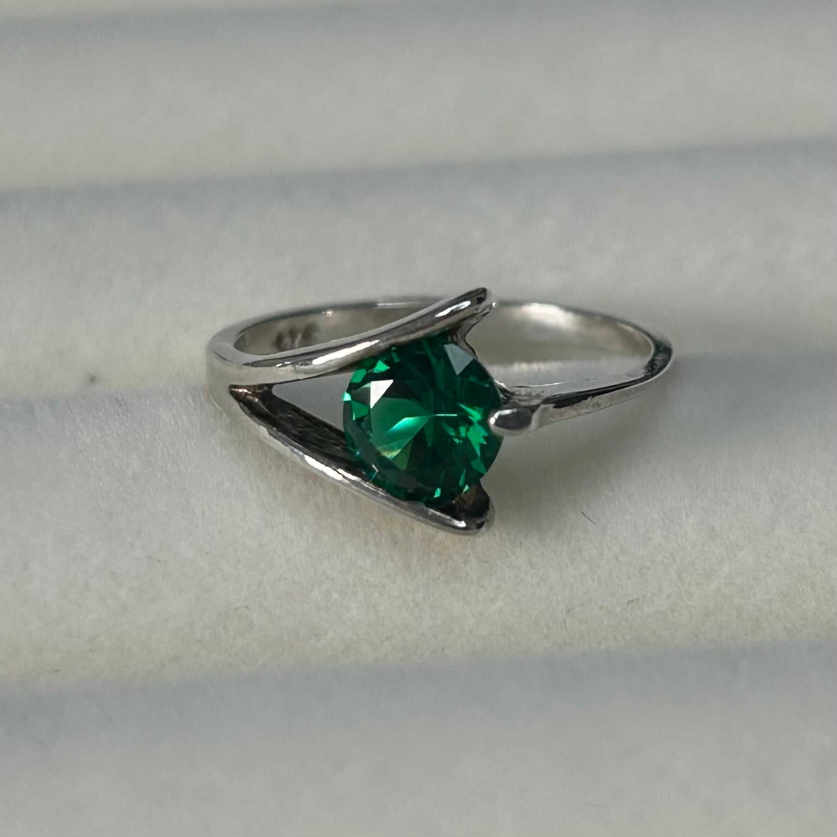 Silver ring with a green gemstone on a light gray background
