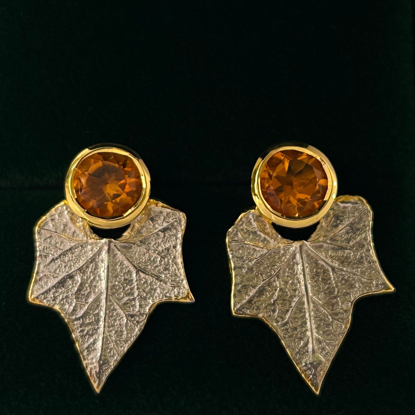 Pair of earrings with leaf design and amber-colored gemstones on a black background