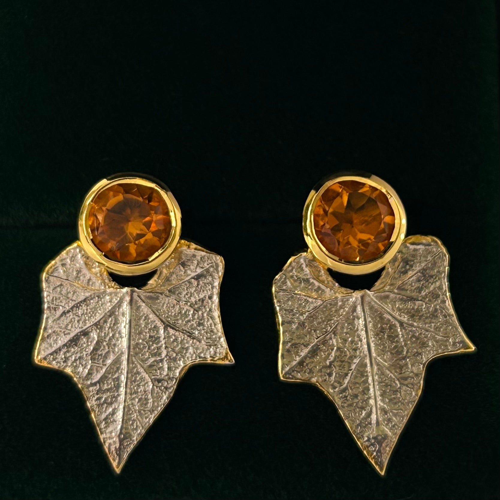 Pair of earrings with leaf design and amber-colored gemstones on a black background