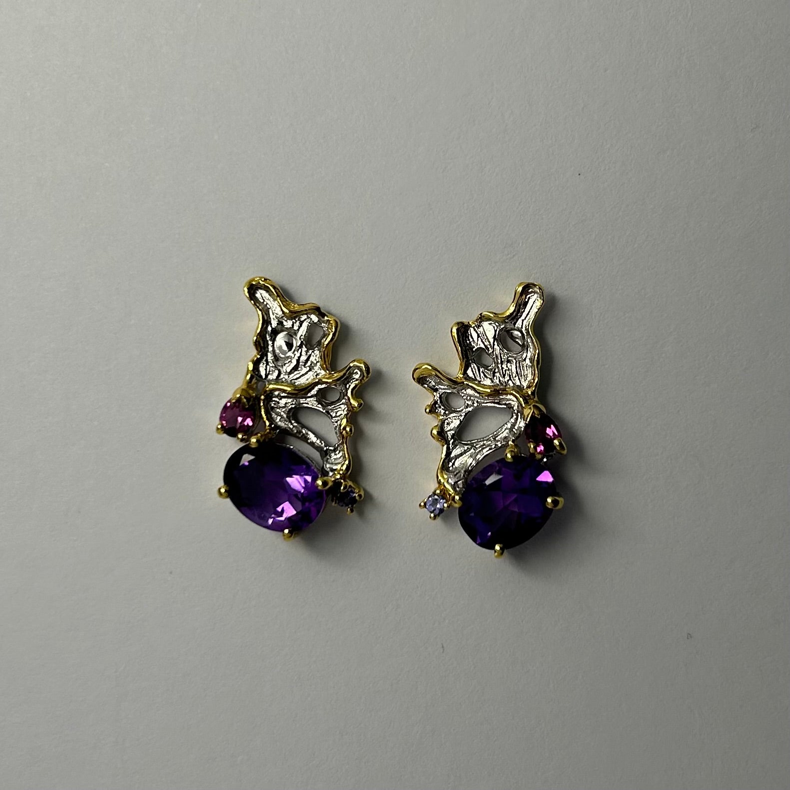 Pair of gold and silver earrings with purple amethyst gemstones on a light gray background