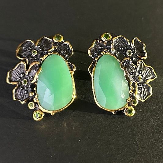 Pair of earrings with green teardrop stones and gold floral designs on a black background