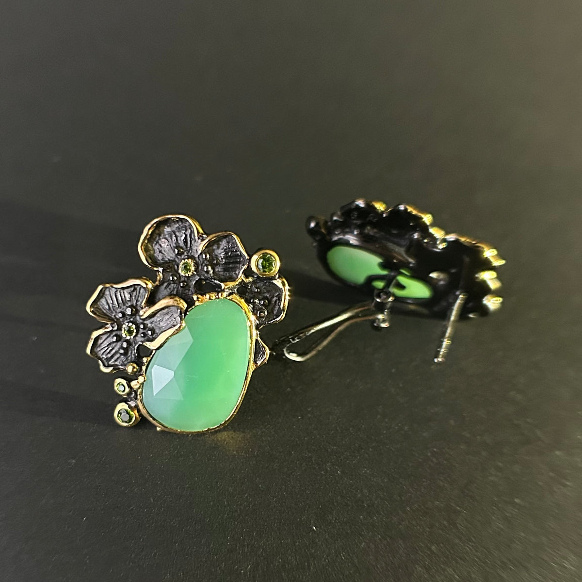 Pair of silver earrings with green chyroprase gemstones and floral designs on a gray background