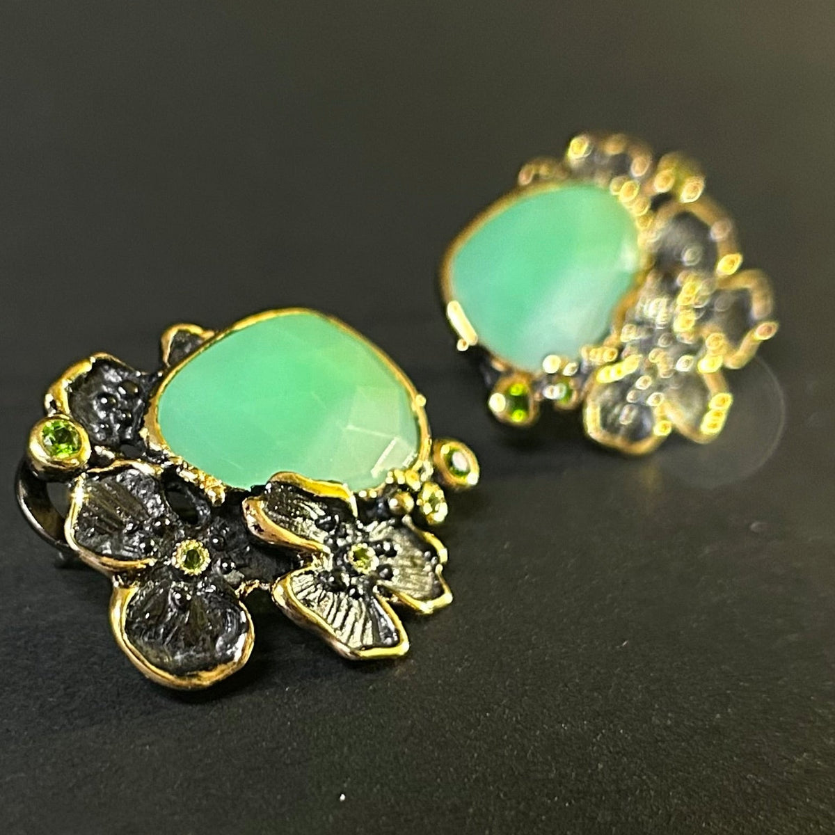 Pair of silver earrings with green chyroprase gemstones and floral designs on a gray background