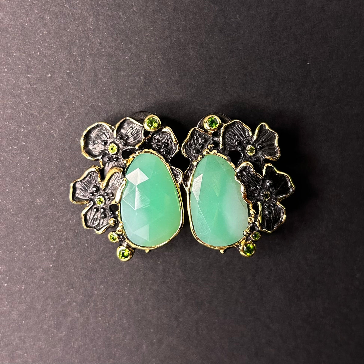 Pair of silver earrings with green chrysoprase gemstones and floral designs on a gray background