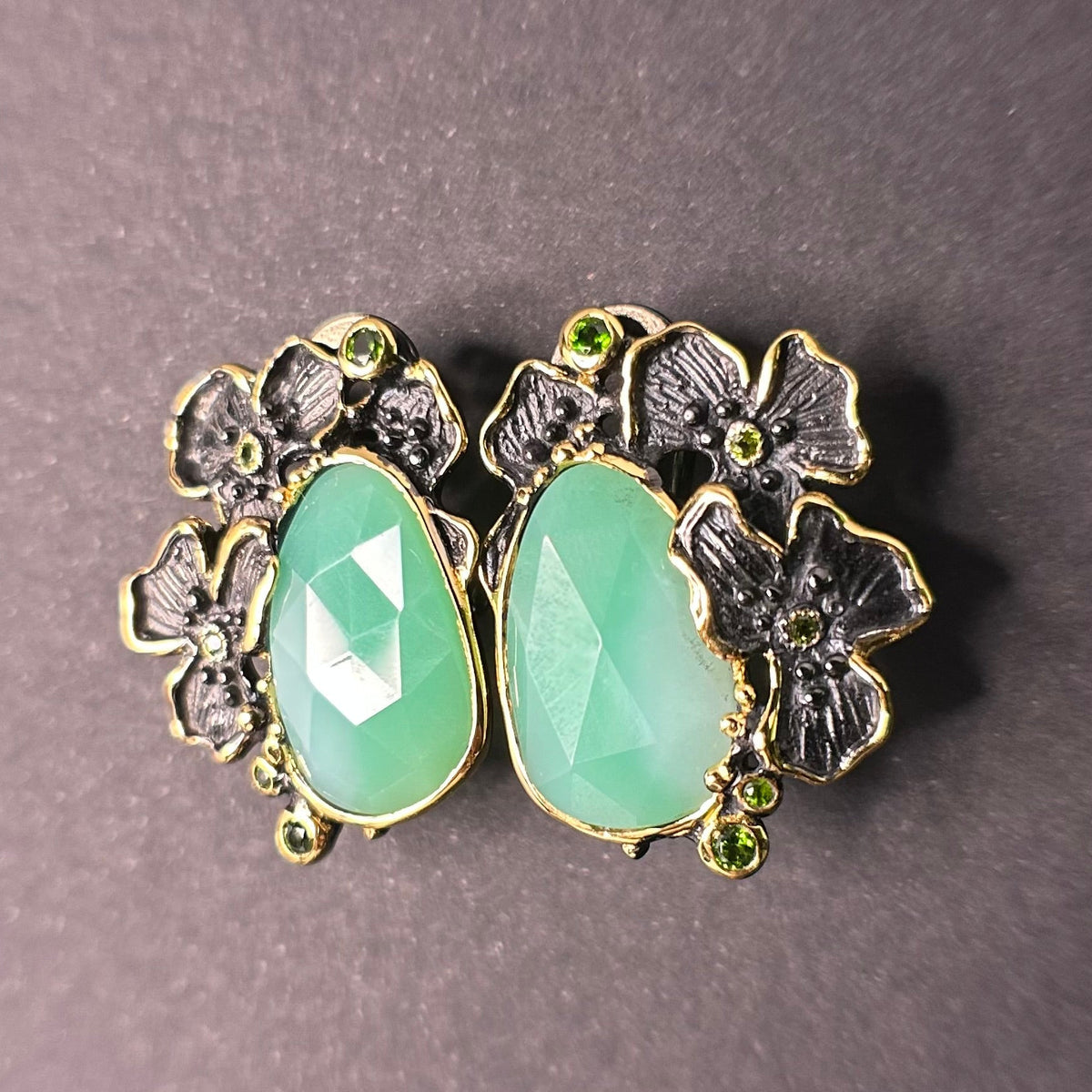 Pair of silver earrings with green chrysoprase gemstones and floral designs on a gray background