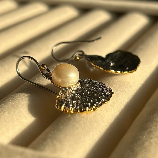 Pair of earrings with a pearl and silver textured design on a textured surface.