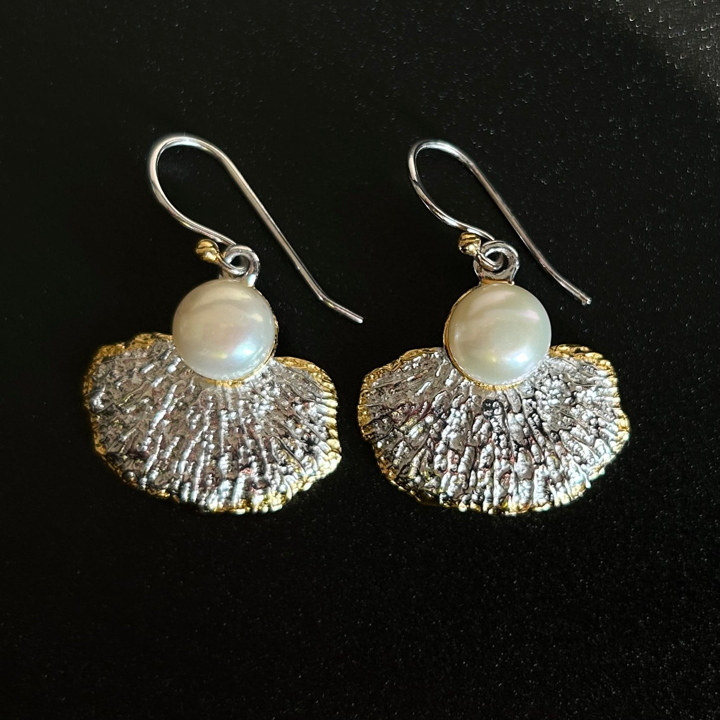 Pair of earrings with textured silver fans and pearl beads on a black background