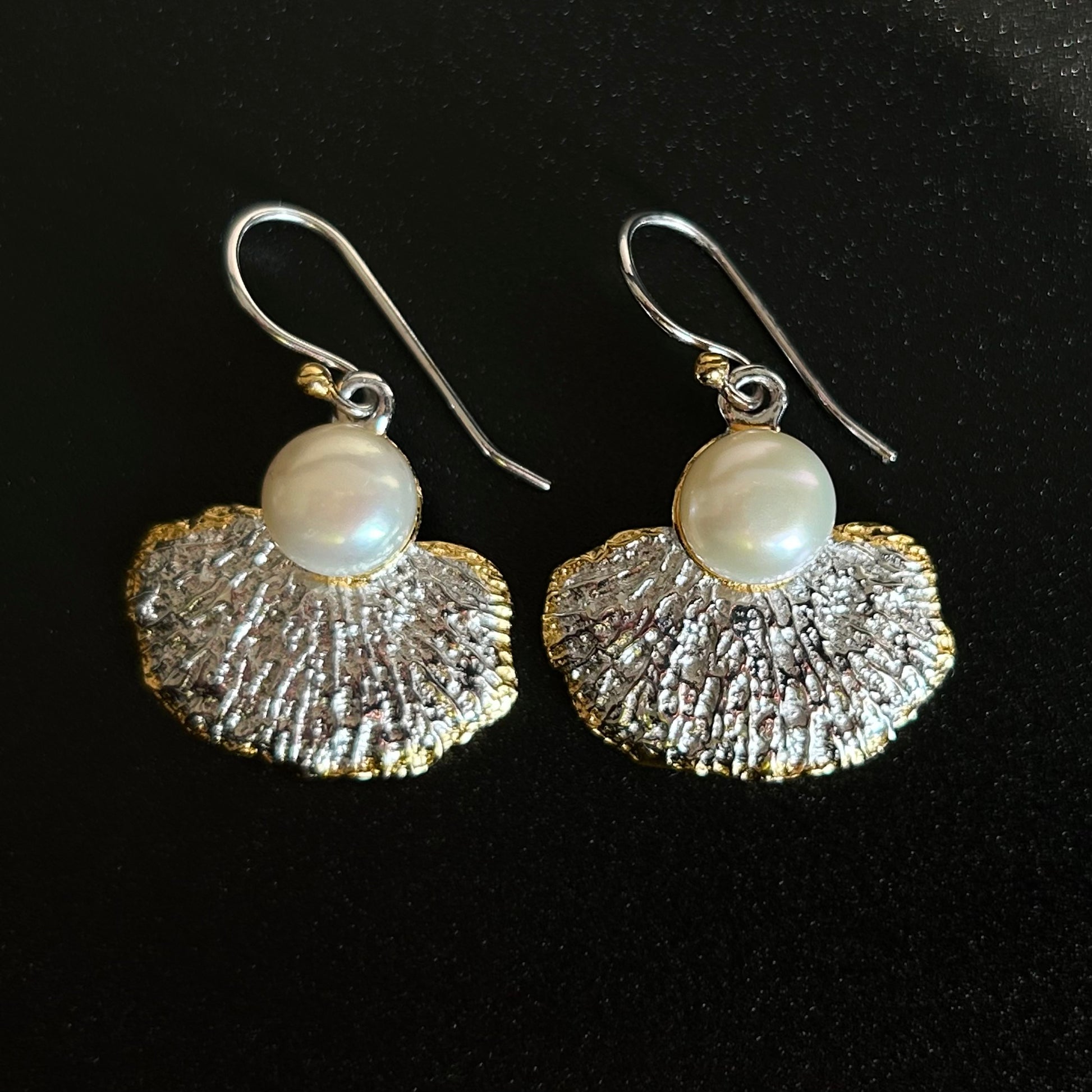 Pair of earrings with textured silver fans and pearl beads on a black background
