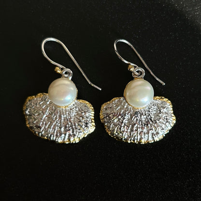 Pair of earrings with textured silver fans and pearl beads on a black background
