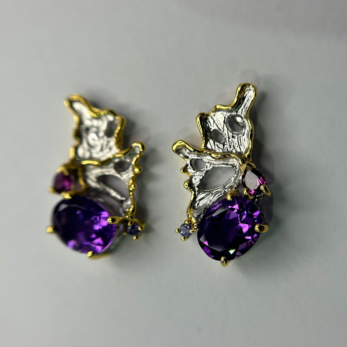 Pair of silver gold earrings with purple amethyst gemstones on a gray background