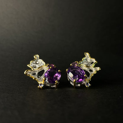 Pair of earrings with purple gemstones and gold accents on a black background