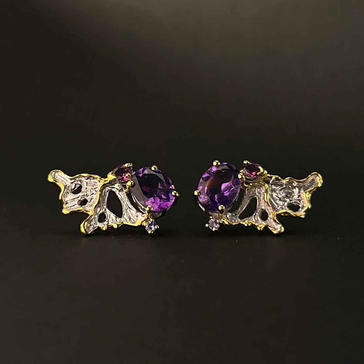 Pair of gold and purple gemstone earrings on a black background