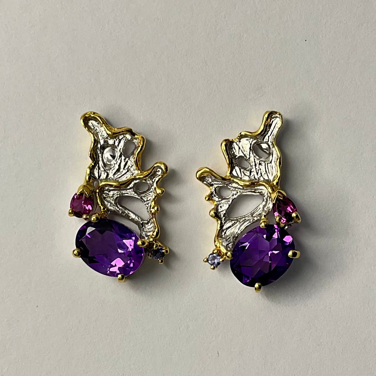 Pair of gold and silver earrings with purple amethyst gemstones on a light gray background