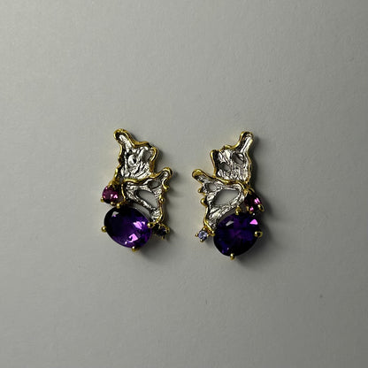 Pair of gold and silver earrings with purple amethyst gemstones on a light gray background