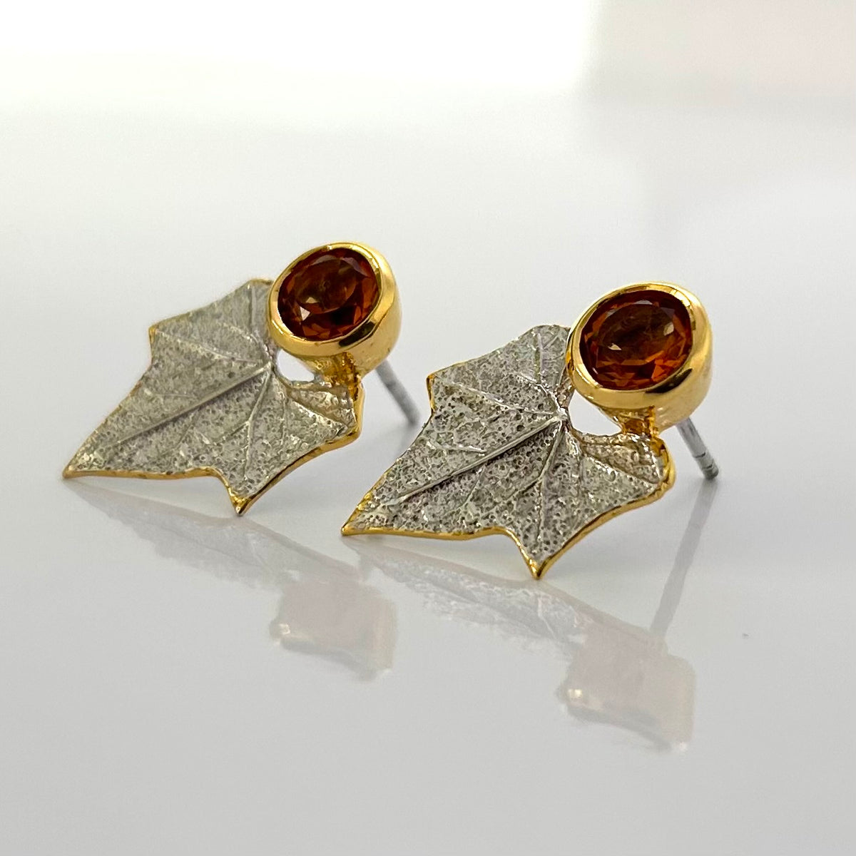 Pair of silver earrings with leaf design and brown citrine gemstones on a white background
