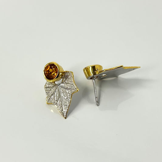 Gold and silver leaf-shaped earrings on a light gray background