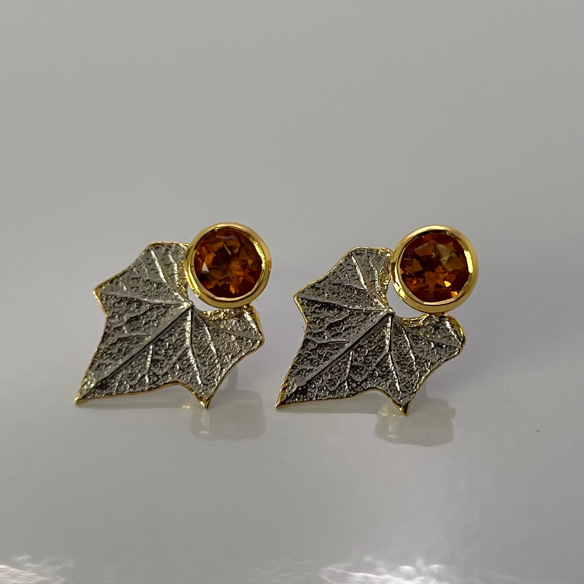Pair of sterling silver earrings with leaf design and amber-colored citrine gemstones on a gray background