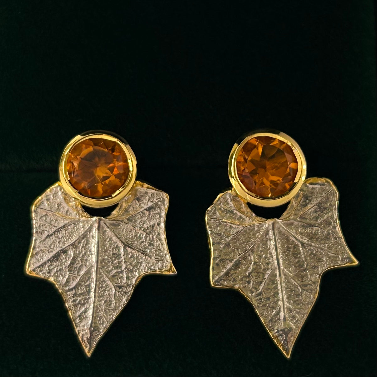 Pair of earrings with leaf design and amber-colored gemstones on a black background