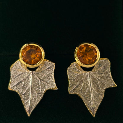 Pair of earrings with leaf design and amber-colored gemstones on a black background