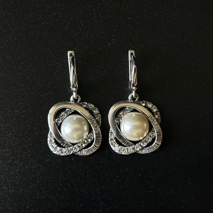 Pair of silver earrings with pearl centers on a black background