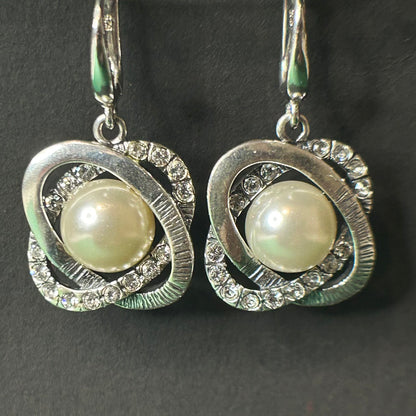 Pair of silver earrings with pearl and gemstone accents on a dark background