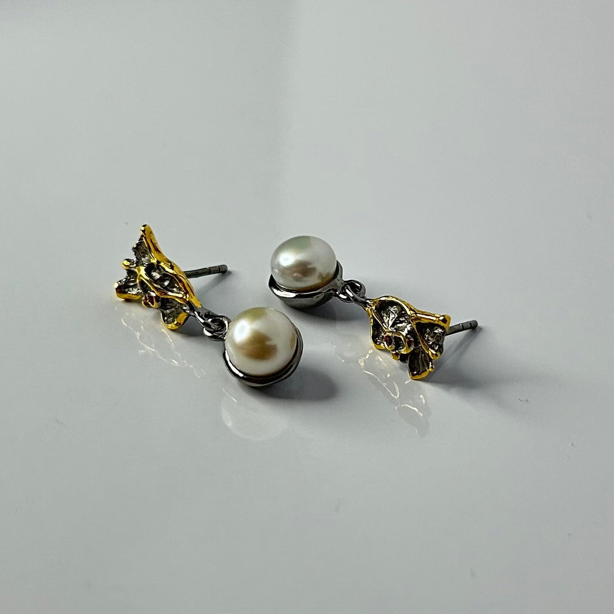 Pair of pearl earrings with gold and silver accents on a light gray background