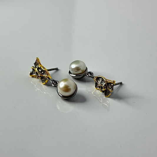 Pair of pearl earrings with gold and silver accents on a light gray background