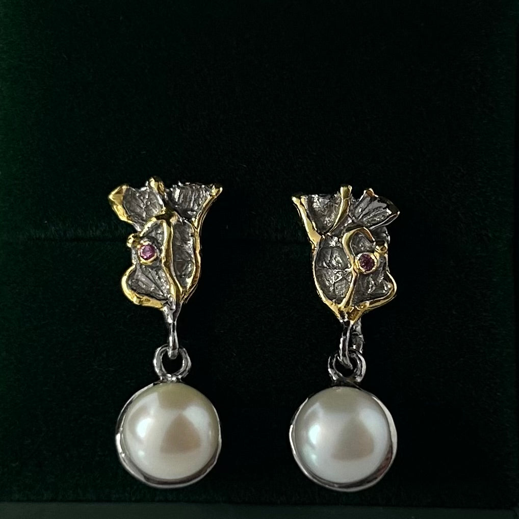 Pair of earrings with floral designs and pearl drops on a green background