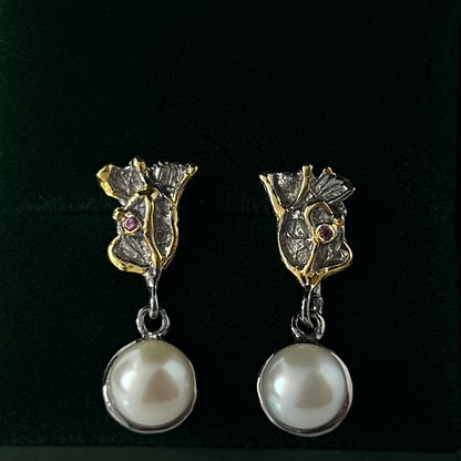 Pair of earrings with floral designs and pearl drops on a green background