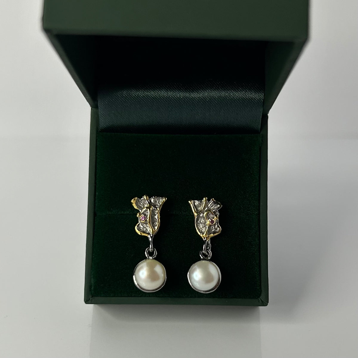 Pair of pearl earrings in a green jewelry box on a light gray background