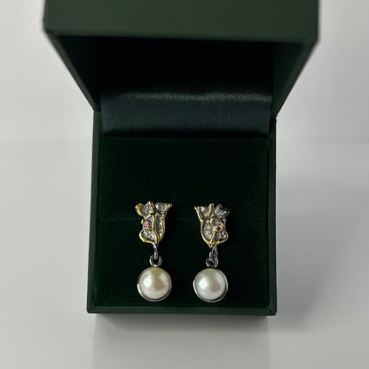 Pair of pearl earrings in a green jewelry box on a light gray background