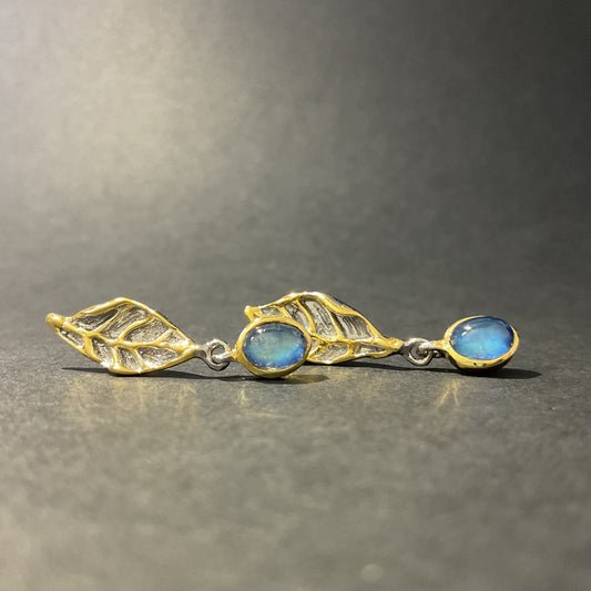 Silver and gold earrings with blue stones on a gray background