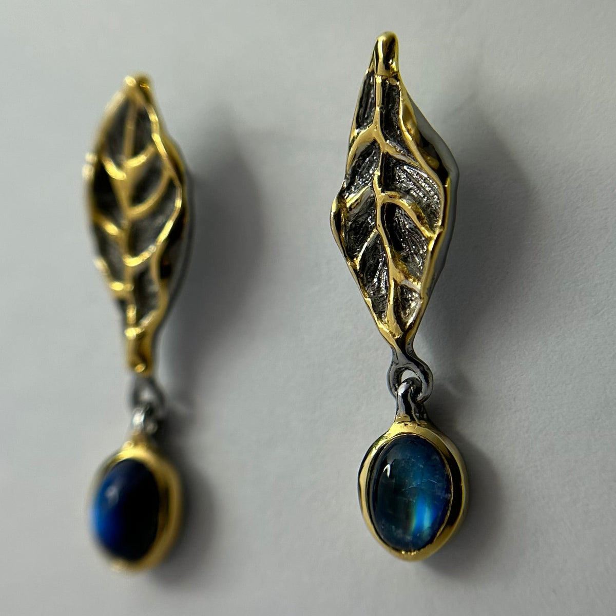 Pair of gold and silver leaf-shaped earrings with blue stones on a gray background