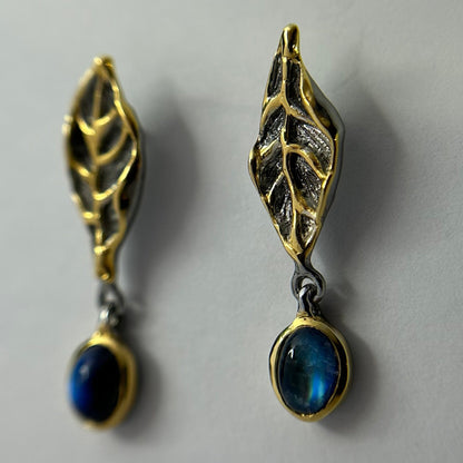 Pair of gold and silver leaf-shaped earrings with blue stones on a gray background