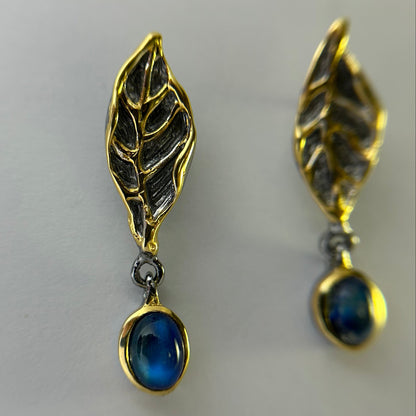 Gold and silver leaf-shaped earrings with blue gemstones on a light gray background