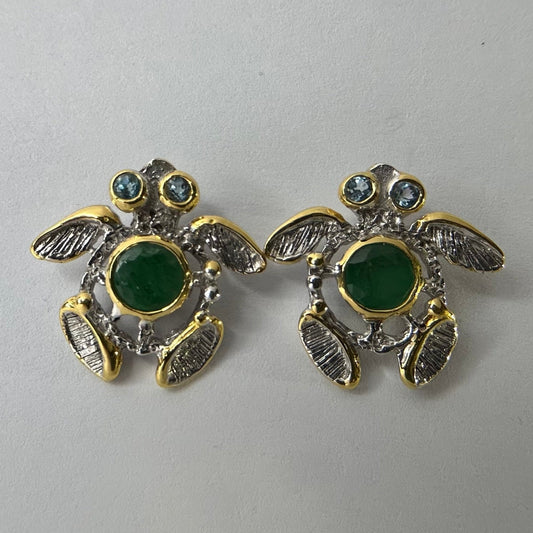 Turtle-shaped silver earrings with green emerald gemstones on a light gray background