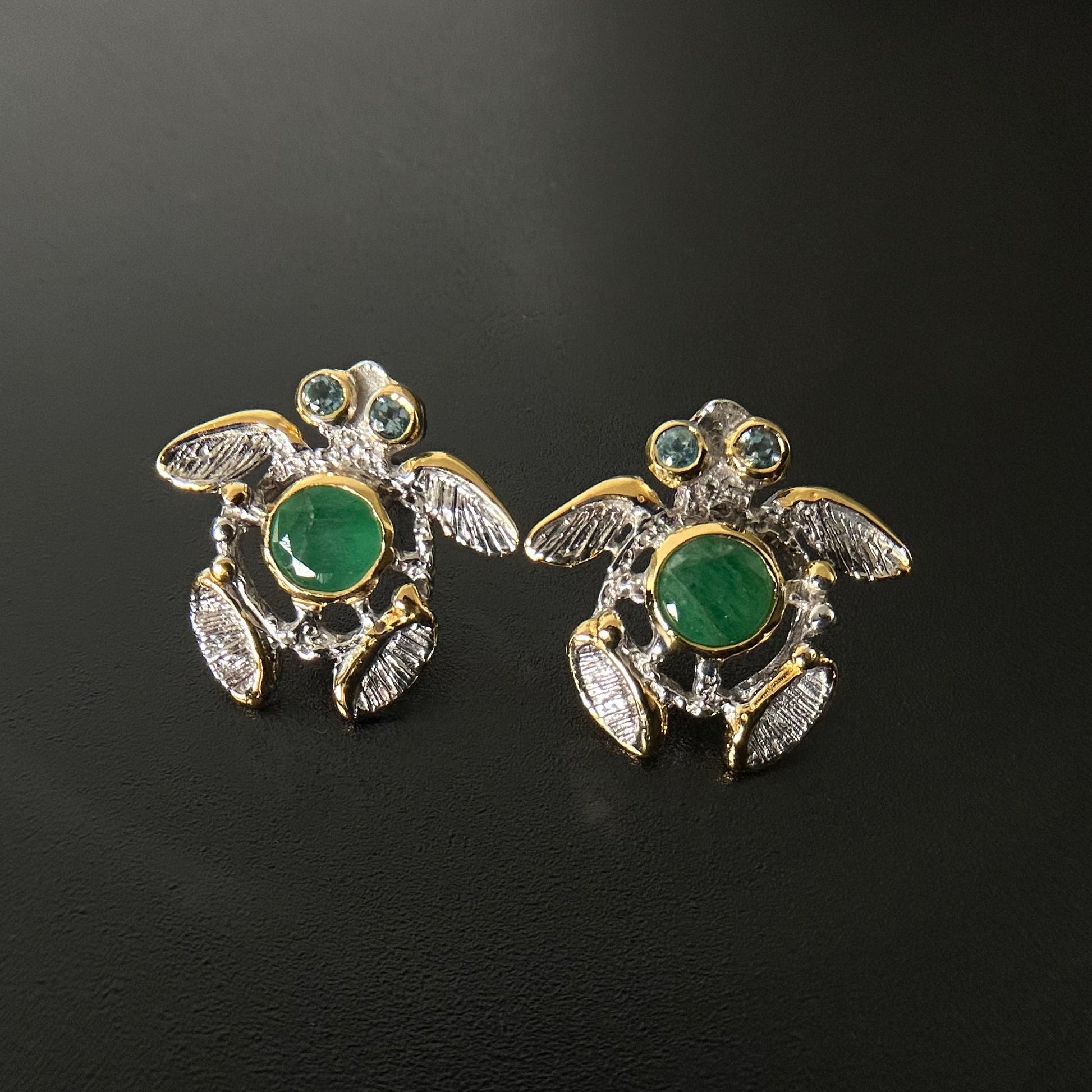 Turtle-shaped earrings with green gemstones on a black background
