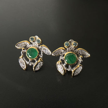 Turtle-shaped earrings with green gemstones on a black background