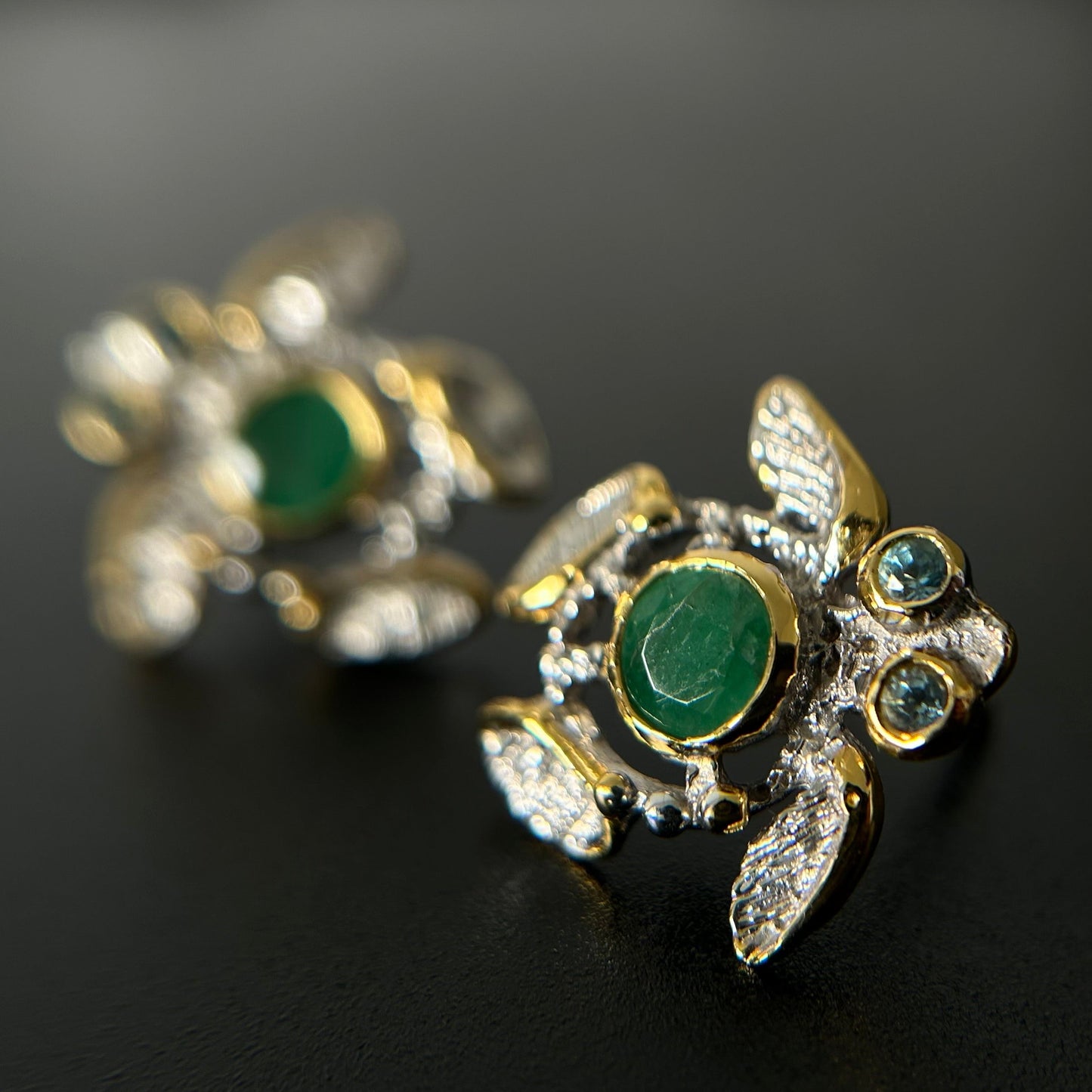 Gold silver turtle-shaped earrings with green emerald stones on a black background